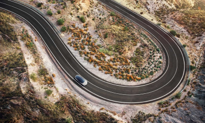 Aerial view of Lexus concept vehicle driving around a winding U-shaped road, shrubbery surrounds it.