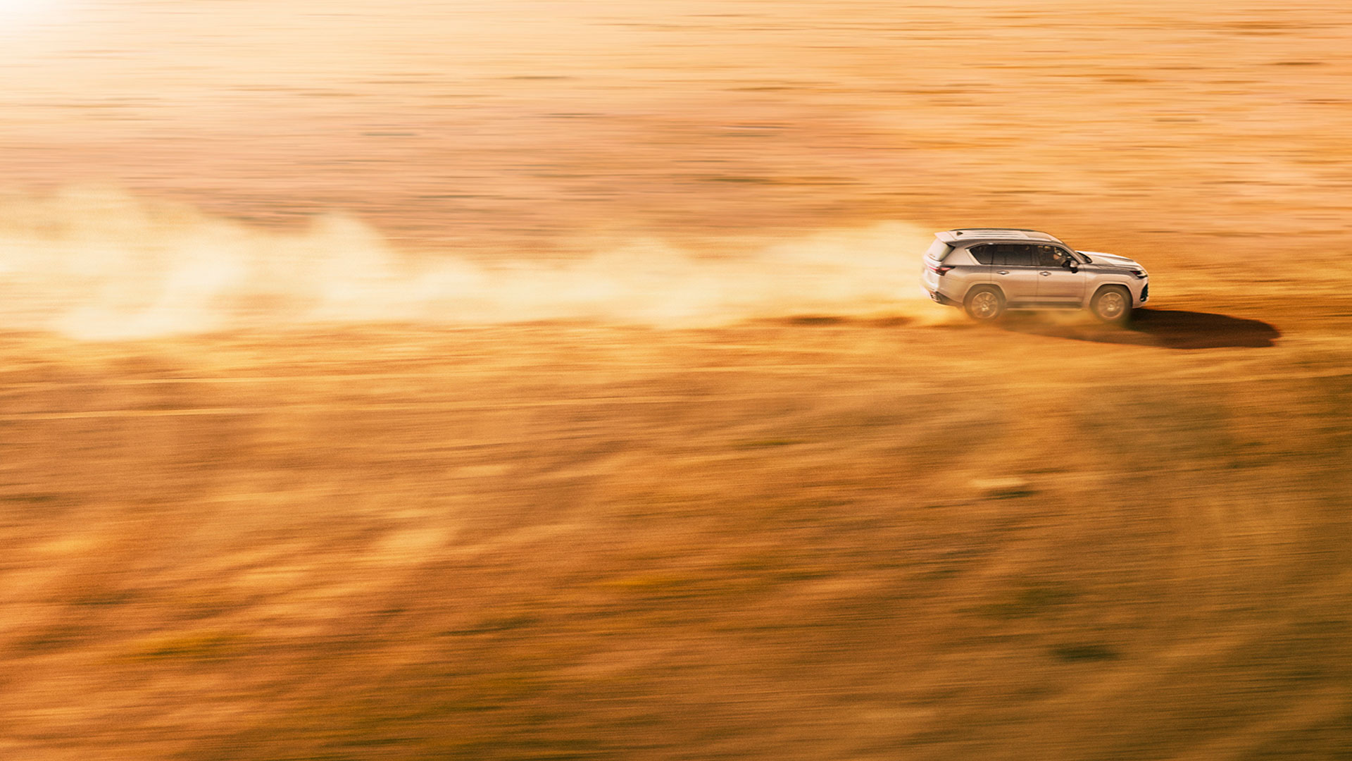 Lexus LX driving through a desert with a dust cloud billowing behind it