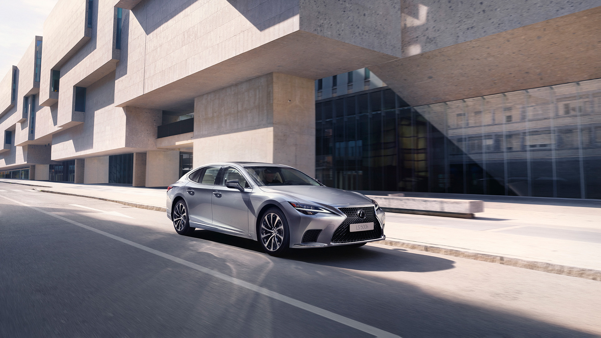 A lexus LS is parked next to a modern looking building with angular architecture.